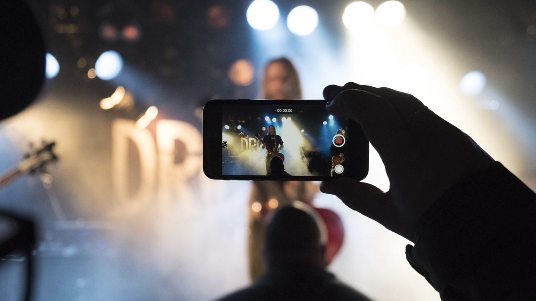 A viewer recording a video of a concert with a phone.