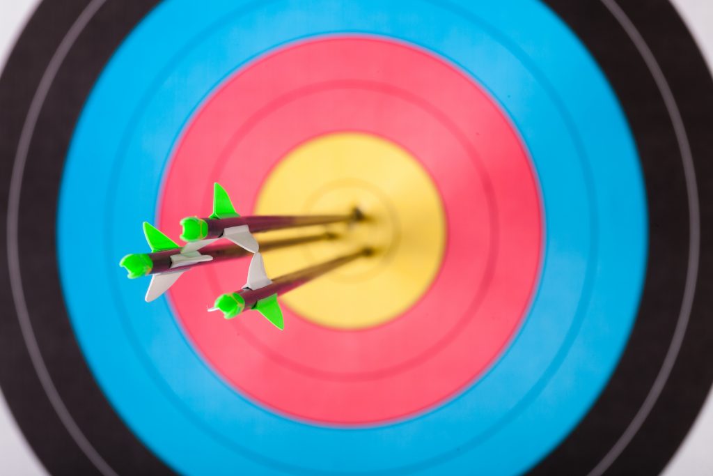 Archery target with three arrows in the bullseye.